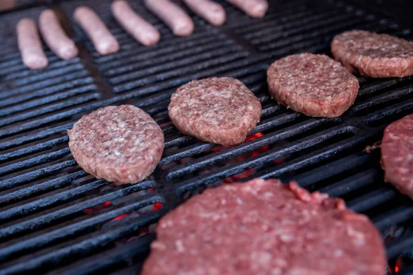 Kiełbasy i hamburgery gotowanie na grillu.Mięso gotowanie na grillu, selektywne focus.burger kotlety mięsne pieczenie na grillu na świeżym powietrzu. — Zdjęcie stockowe