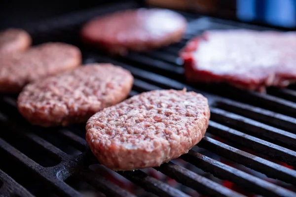 Surowe hamburgery wołowe z odrobiną soli i pieprzem na grillu. przygotowane mięso do grillowania.Raw kotlety burger. Okrągłe paszteciki surowego mięsa mielonego palonego na metalowej siatce. — Zdjęcie stockowe