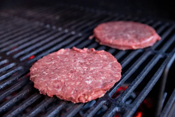 Surowe hamburgery wołowe z odrobiną soli i pieprzem na grillu. przygotowane mięso do grillowania.Raw kotlety burger. Okrągłe paszteciki surowego mięsa mielonego palonego na metalowej siatce. — Zdjęcie stockowe