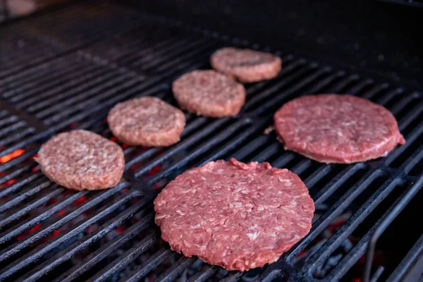 Surowe hamburgery wołowe z odrobiną soli i pieprzem na grillu. przygotowane mięso do grillowania.Raw kotlety burger. Okrągłe paszteciki surowego mięsa mielonego palonego na metalowej siatce. — Zdjęcie stockowe