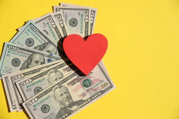 Amerikan dolarlarında kırmızı kalbin en üst görüntüsü, sarı arka plan. Para yerine para yerine kırmızı kalp kullanılıyor. Nakit para, kopyalama alanı. Tasarruf planı veya sağlık sigortası kavramı.