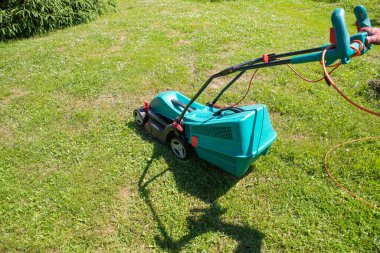 Bahçe biçen yaşlı bir adam. Parlak yeşil çimlerde mavi çim biçme makinesi. Bahçesinde çim biçme makinesiyle çim biçen bir adam.