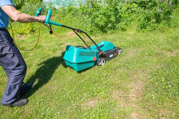 庭を刈るシニア男性明るい緑の草の中に青い芝生の芝刈り機。芝生の芝刈り機で庭の草を刈る男. — ストック写真