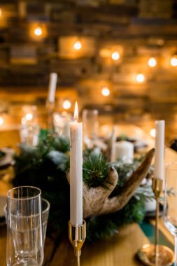 Şarap kadehleri ve noel ışıklarıyla süslü bir Noel sofrası. Kış süslemeleri ve beyaz mumlar arasında şenlik masası. Aile yemeği. Yeni yıl süsleri ahşap masada.