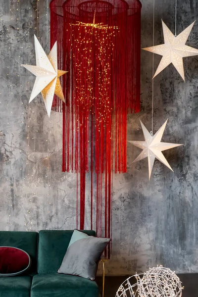 twinkle star lamp on grey wall.christmas mood. Living room interior. Stilysh and creative festive decor for winter holidays.Hanging star lantern lights for holiday. Modern lamp with long red threads