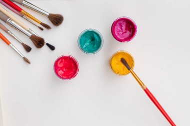 Beyaz zemin üzerinde gouache kavanozları, düz kompozisyon, üst görünüm. Kopya alanı. Gouache renkleri ve boya brushi ile düz kompozisyon. Resim ve çizim dersleri için ana sınıfların reklamları