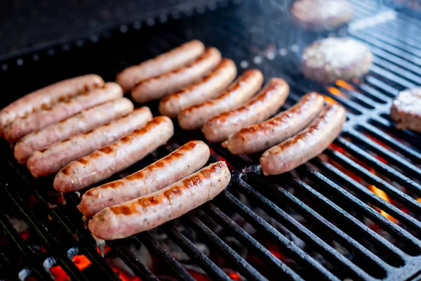 Kiełbaski wieprzowe grillujące na przenośnym grillu z jedną kiełbasą obracaną w parę szczypiec na letnim pikniku, zbliżenie grilla, mięsa i ognia — Zdjęcie stockowe