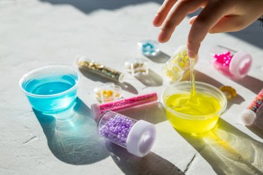 Beyaz arka planda tek başına el yapımı sarı sümüklü çocuk sümük, sümük ve sümük yapmak için aksesuarlar. Küçük kız masada ev yapımı balçık oyuncağı yapıyor.