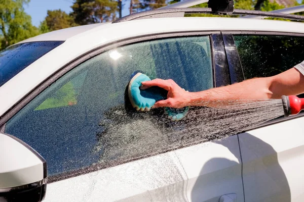 Benvit bil tvätt på öppen luft.Manliga händer hålla med blå svamp tvättbil.Tvål suger, bubblor och handske. — Stockfoto