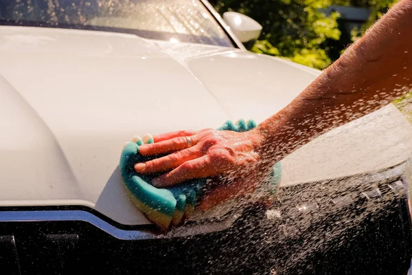 Benvit bil tvätt på öppen luft.Manliga händer hålla med blå svamp tvättbil.Tvål suger, bubblor och handske. — Stockfoto