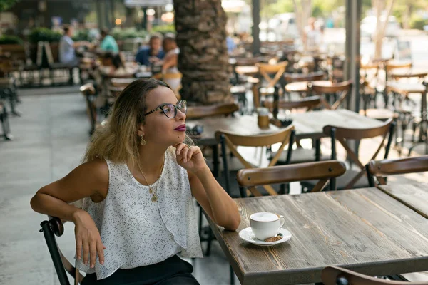 Γυναίκα Κάθεται Ένα Υπαίθριο Καφέ Καπουτσίνο Ένα Ξύλινο Τραπέζι Βλέπει — Φωτογραφία Αρχείου