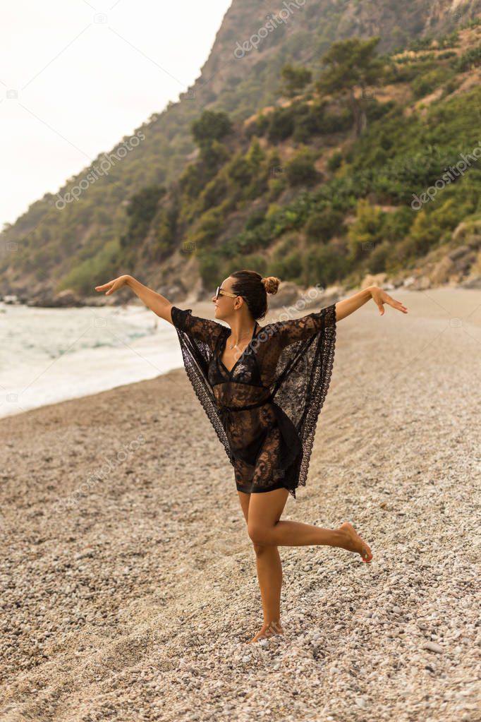 Vertical full lengh portrait of young woman wearing black lace tunic and dancing in a beautiful bay.