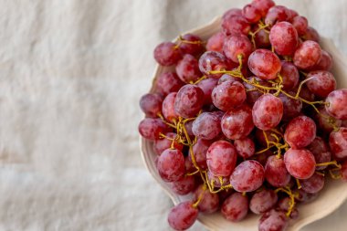 Bir plaka üzerinde ışık gri keten masa örtüsü kırmızı üzüm ile üst görünüm vurdu. Yatay kompozisyon. Kopya alanı.