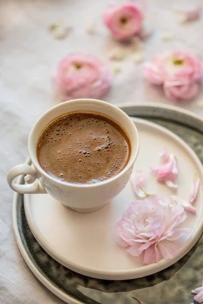 Spring concept. A cup of black coffee with pink ranunculus aroung it. Vertical composition.