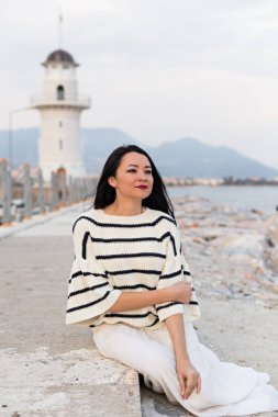 Deniz feneri yakınında oturan deniz tarzı giysiler kadın