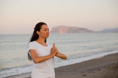 Kadın, plajda yoga ve meditasyon yapıyor.