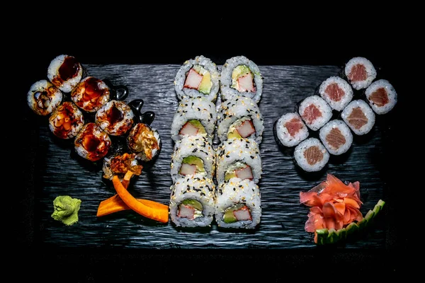 zencefil ve wasabi ile süslenmiş siyah seramik bir tabak üzerinde sunulan suşi rulo farklı türde bir seçim 