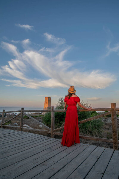 A female model posing in a red dress during sunrise along the coastline of the Mediterranean