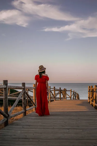a female model with her back turned walking down wooden decking to the sea during sunset