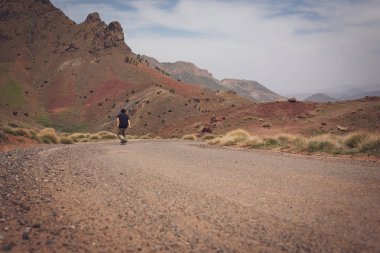 güneşli bir günde tepeler arasında yolda paten sürme rahat giysiler içinde kaykaycı geri görünümü