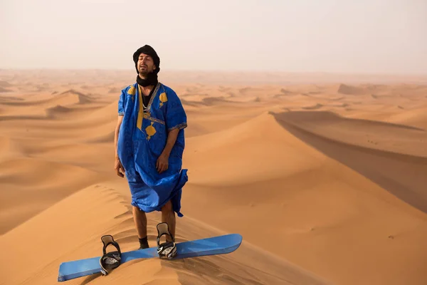 Sandboarder Erg Cheggaga, Fas kumul üstüne kum kurulu ile ayakta iken zevk Touareg Gandoura giymiş 