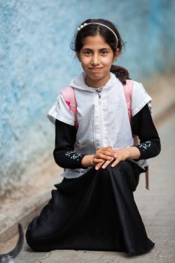  sırt çantası kamera bakarak ve eski sokakta gülümseyen sevimli küçük faslı esmer kız portresi, Fez, Fas   