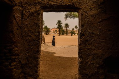 Güneşli bir günde eski Arap şehrinde binaların arasında yürüyen koyu renk elbiseli bir kızdan manzara  