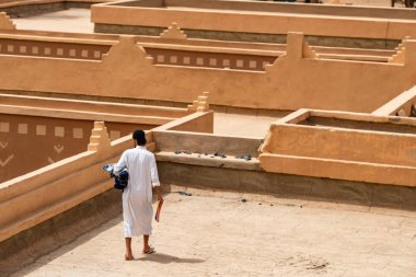 Elinde giysiler ve defterler olan bir adam güneşli bir günde geleneksel Arap şehrinin çatısında yürüyor. 