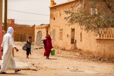 Geleneksel Arap elbiseli kadınlar ve güneşli bir günde eski caddede yürüyen adam, Fas