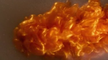 Parlak boya. Akrilik sıvı. Bulanık turuncu mor renkli su tanecikleri soyut arka planda süzülen girdap buharı..