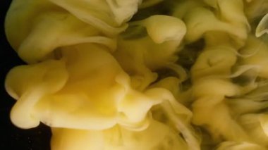 Sis karışımı. Sıvı pigmenti. Bulanık sarı mürekkep rengi duman dalgası soyut koyu siyah arkaplanda yüzen akrilik parçacıklar..