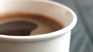 Kremalı, beyaz köpüklü, dumanı tüten sıcak kahvenin üstünde kıvrılıp duran, el değmemiş beyaz kağıt bardakta karmaşık desenler oluşturan.