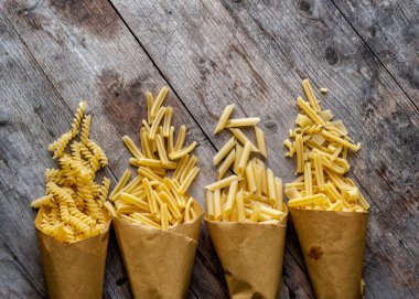 Tahta bir arka planda kağıt torbalarda çiğ makarna. Üstten bak. Doğal ışıkla çekilmiş..