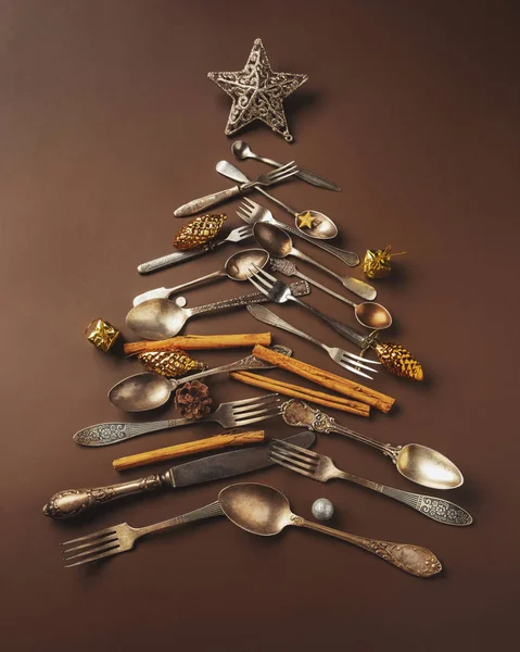 Abstract kerstboom gemaakt van bestek op een donkere, bruine achtergrond. Bovenaanzicht. boom van messen en vorken met een ster — Stockfoto