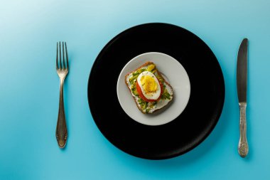 Yumurta ve mavi arka plan, üstten görünüm üzerinde beyaz bir plaka üzerinde avokado sandviç