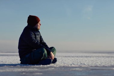 genç bir adam kışın kar buz üzerinde oturur ve güneşe benziyor.