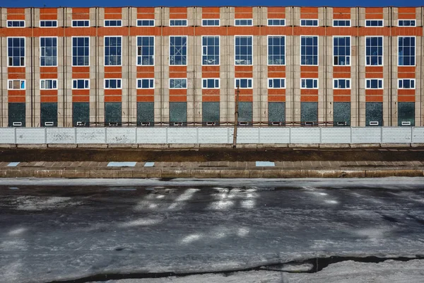 Frozen river and bright orange building. Ice during a thaw in an urban environment