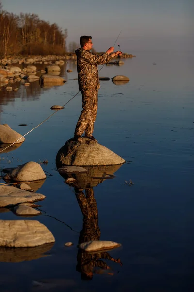Homem captura peixe em pé sobre pedras na água — Fotografia de Stock