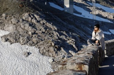 Kız dağların arka planında oturuyor. Bir şapka ve güneş gözlüğü karlı dağların arka plan karşı.