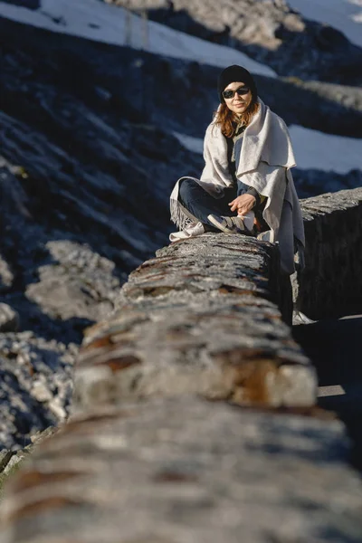 Mladý cestovatel, který sedí na kamenech ve švýcarských Alpách za slunečného dne na pozadí sněhu — Stock fotografie