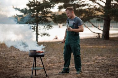 Mutlu adam doğada barbekü et ızgara açık havada pişirir.