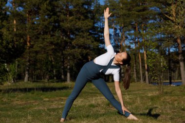 Yoga yapan kadın orman doğasında poz veriyor. Ormandaki çimlerin üzerinde spor yapıyor.