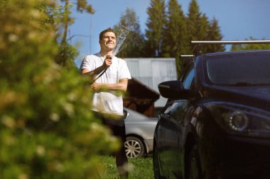 Bir adam arabayı hortumla yıkar. Ülkede aktif dinlenme.