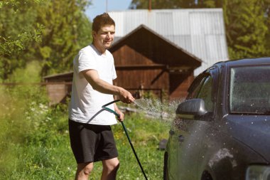 Bir adam arabayı hortumla yıkar. Ülkede aktif dinlenme.