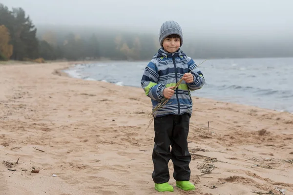 Portrét malého chlapce v bundě na břehu. Dítě na pláži u studeného moře — Stock fotografie