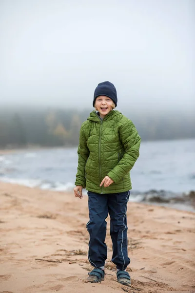 Portrét dívky v bundě na břehu. Dítě na pláži u studeného moře. — Stock fotografie
