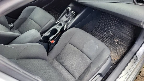 Temizlik servisinden önce arabanın içi. Ön koltuklarında lekeler olan kirli kumaşlı bir araba..