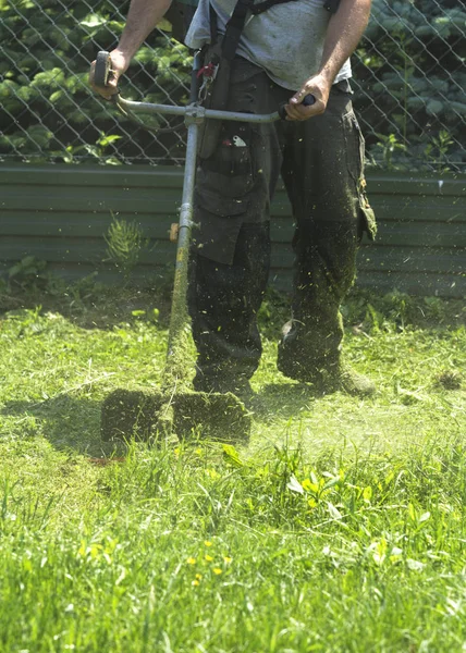 Fırça kesici biçme makinesi veya güç aracı dize çim makası kullanarak adam yeşil biçme yabani ot bu alanın. Düzeltici ile bir çim biçmek için. Trimer bir çim mows. Bir çim bakımı.