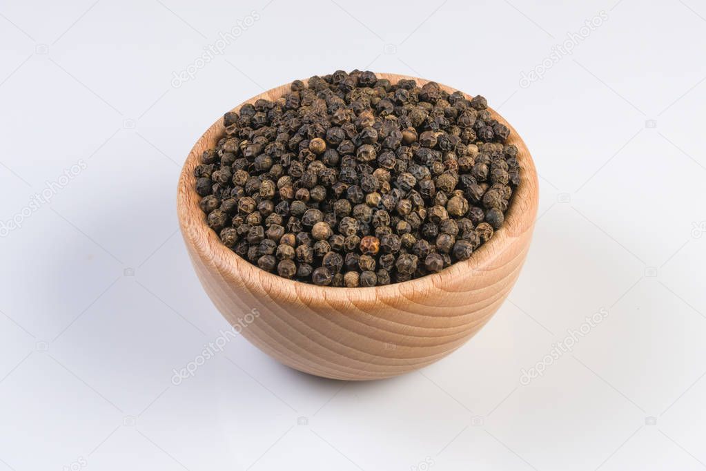 Black pepper peppercorns in wooden bowl isolated on white background. Closeup.