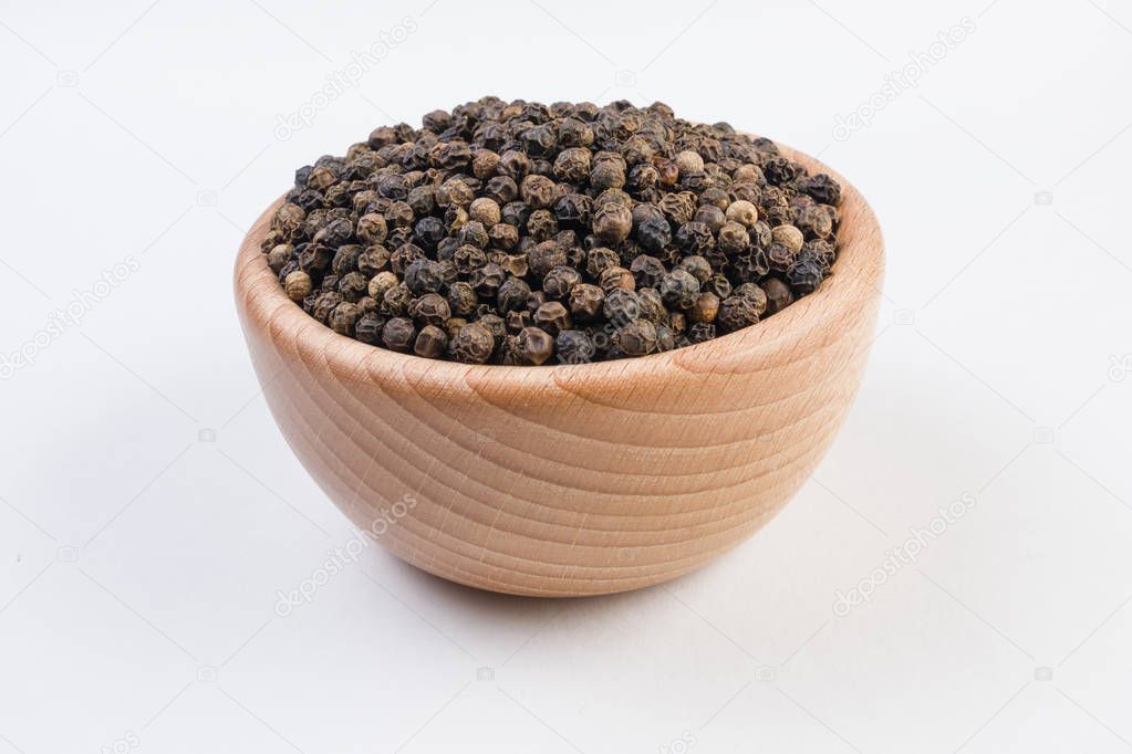 Black pepper peppercorns in wooden bowl isolated on white background. Closeup.